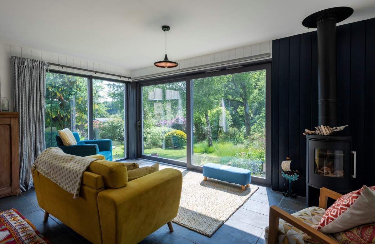 Inside view of Burnside cottage showing wood burner, various furniture and sofa facing glass wall