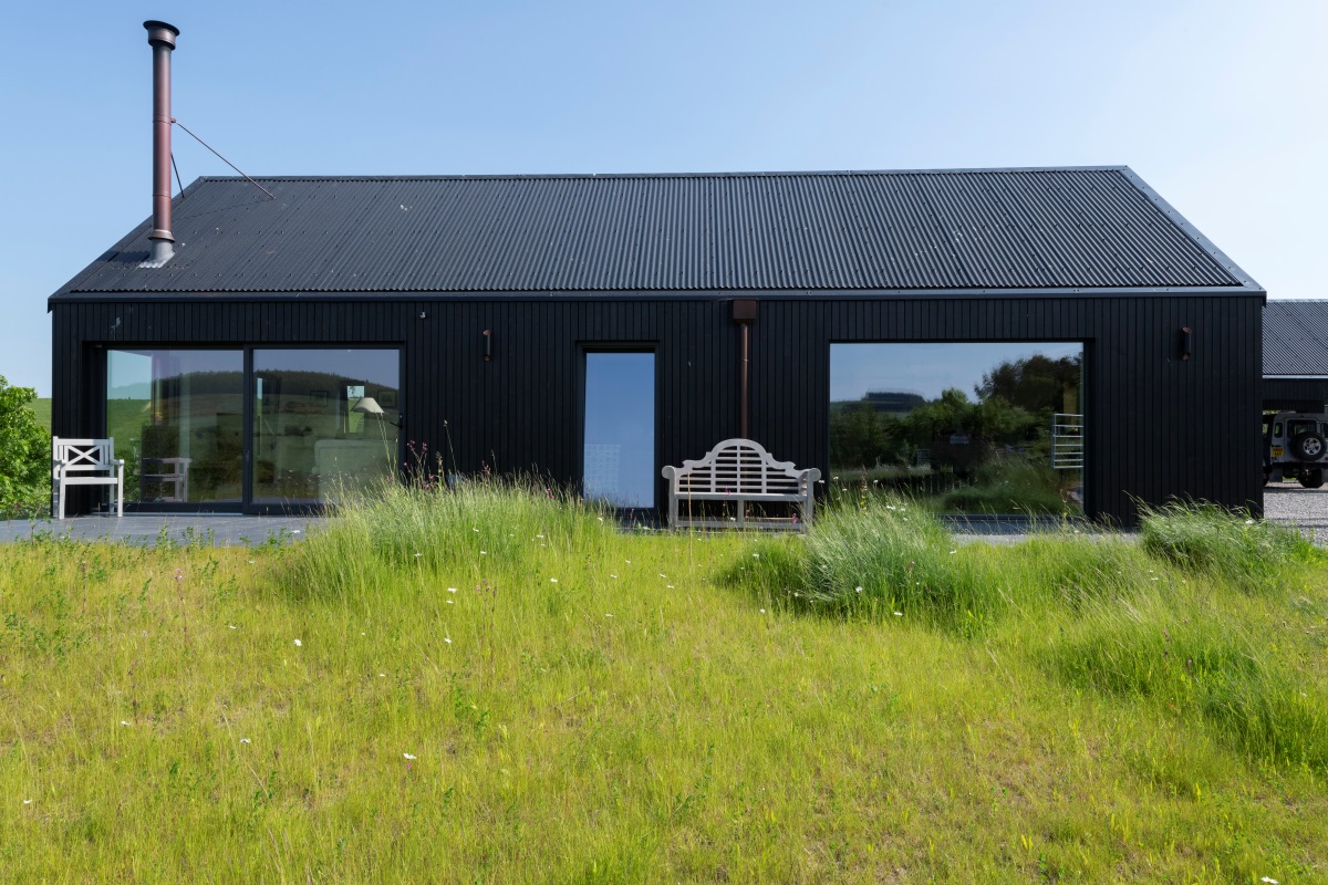 Side view of Camhaniach building with large glass doors, bench and seat, and grass area in foreground